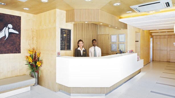 A hotel reception area with a wooden reception desk, two staff members, a menu board, and a wall-mounted artwork. - Hotel 81 Fuji (Singapore)