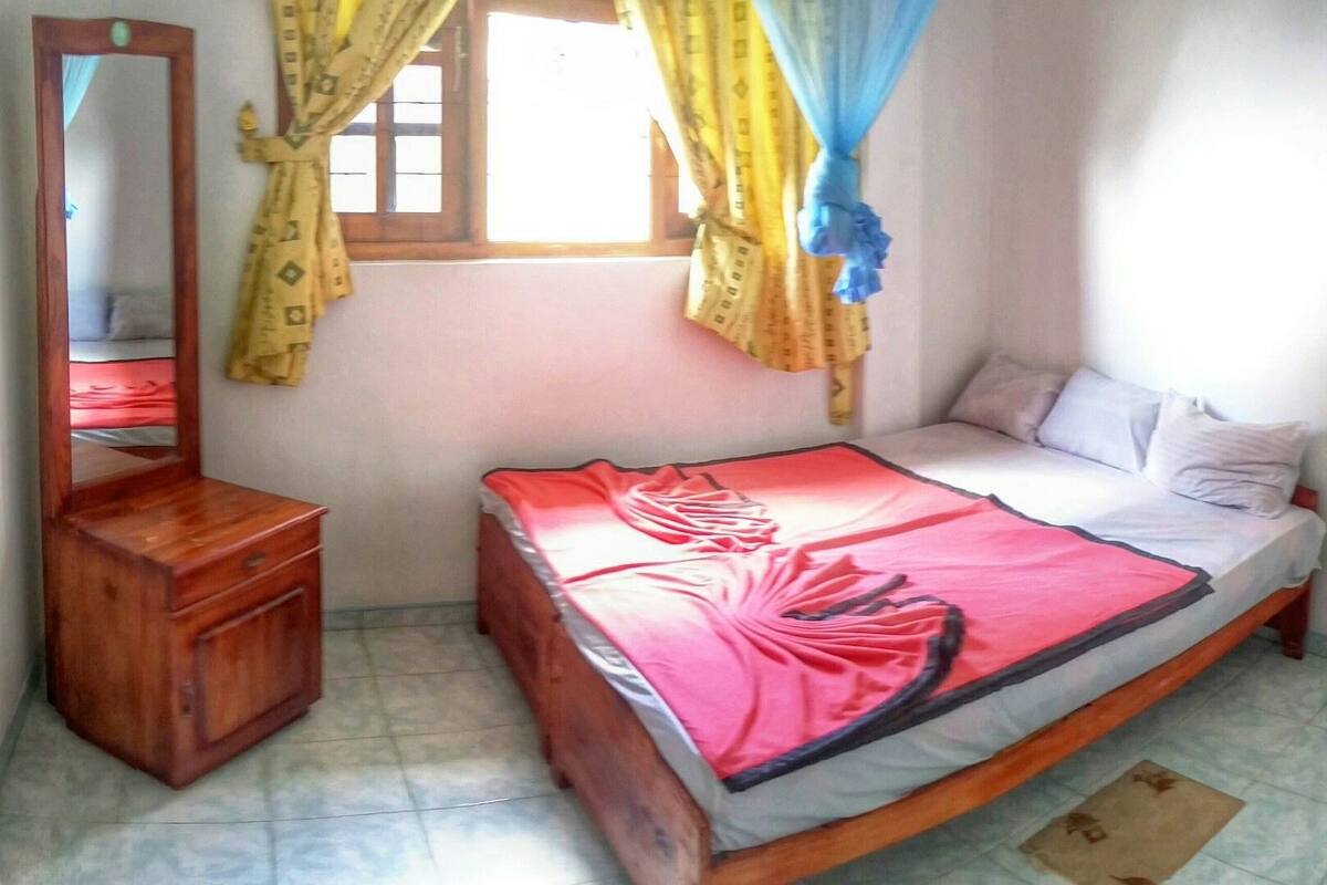 Un dormitorio con una cama, un aparador de madera, un espejo y una ventana con cortinas.