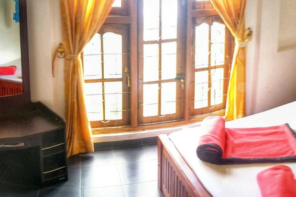 Habitación de hotel con cama, una mesita, una maleta y una ventana con cortinas.