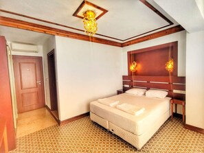 A hotel room with a large bed, wooden headboard, patterned floor, and a ceiling light fixture. - Bozcaada Fahri Hotel (Bozcaada)