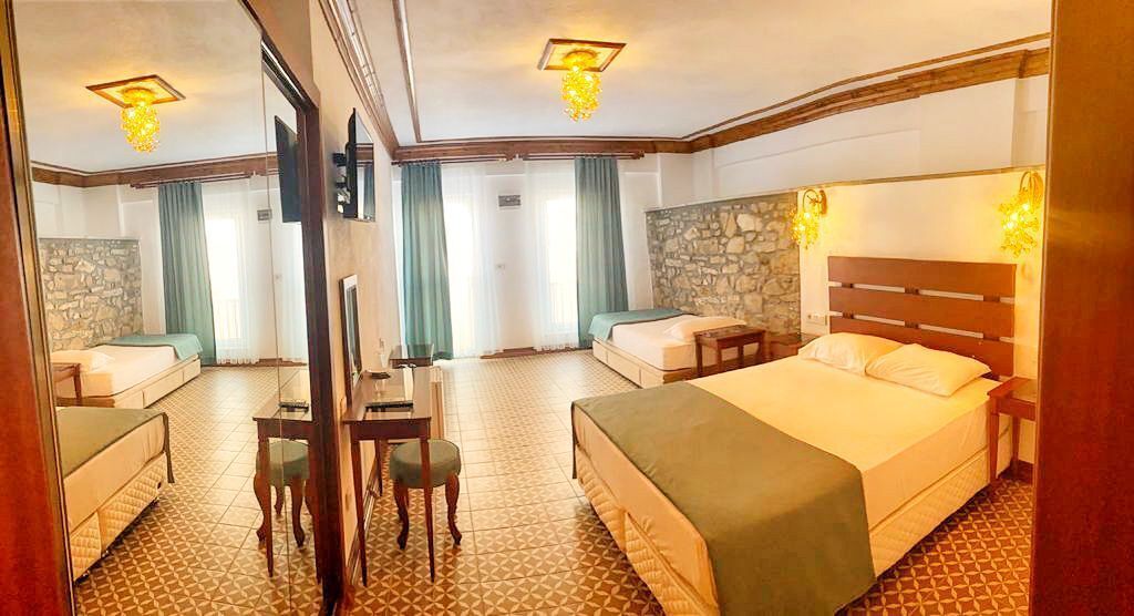 Ein Hotelzimmer mit einem großen Bett, einem Schreibtisch und einem Sessel. Eine Steinsäule und ein Fenster mit Vorhängen sind ebenfalls vorhanden.