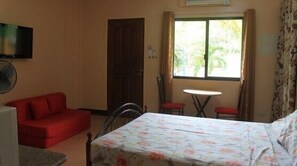 Una habitación con cama, sofá rojo, una mesita y una ventana con cortinas.