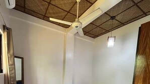 Een slaapkamer met een bed, een plafondventilator, een spiegel en een houten deur.