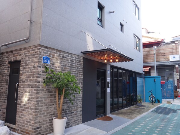 Un edificio moderno con fachada de ladrillo, un árbol en maceta y una puerta azul.