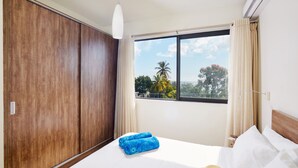 Ein Hotelzimmer mit einem großen Bett, einem Kleiderschrank, einem Fenster mit Blick auf Palmen und einem Deckenventilator.