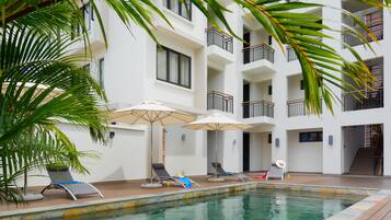 A pool area with lounge chairs and umbrellas, surrounded by a multi-story building with balconies.