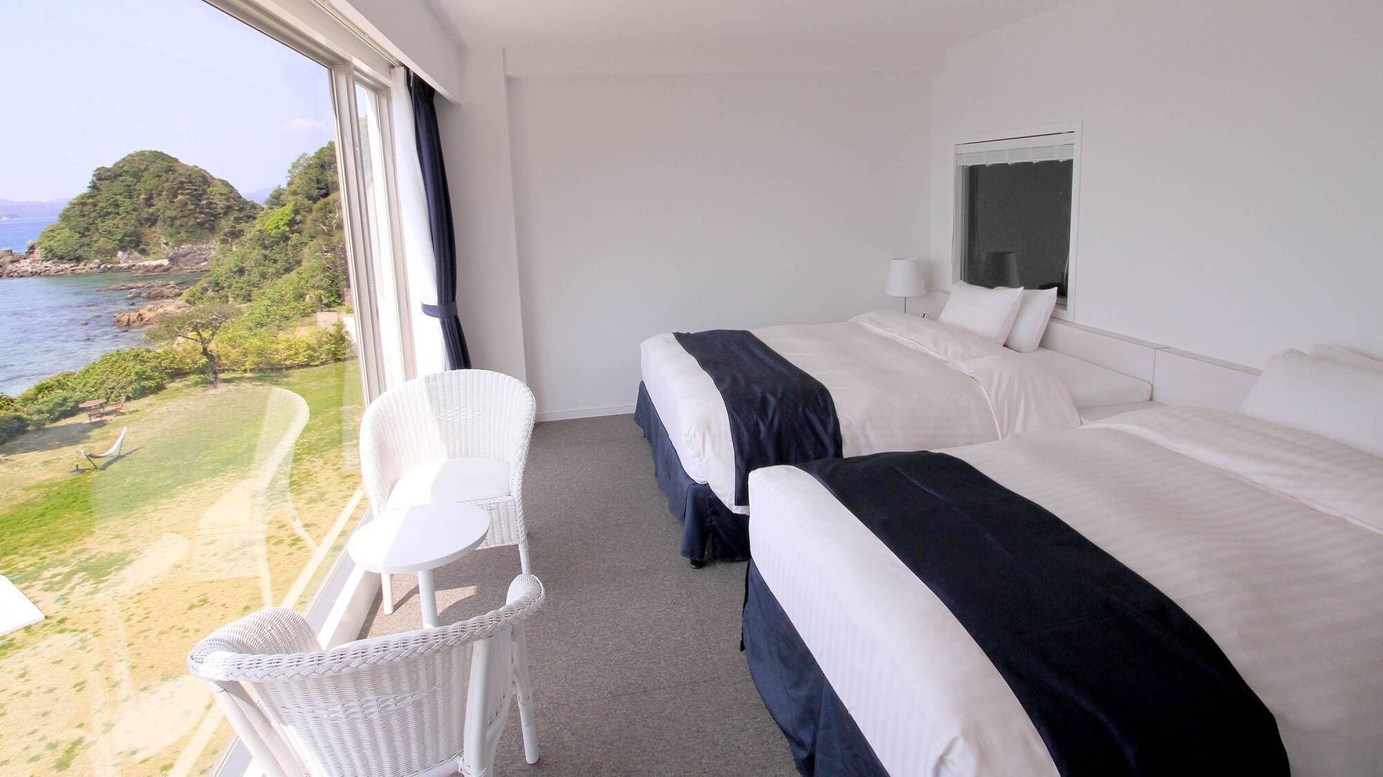A hotel room with two beds, a small balcony chair, and a view of the sea and greenery.