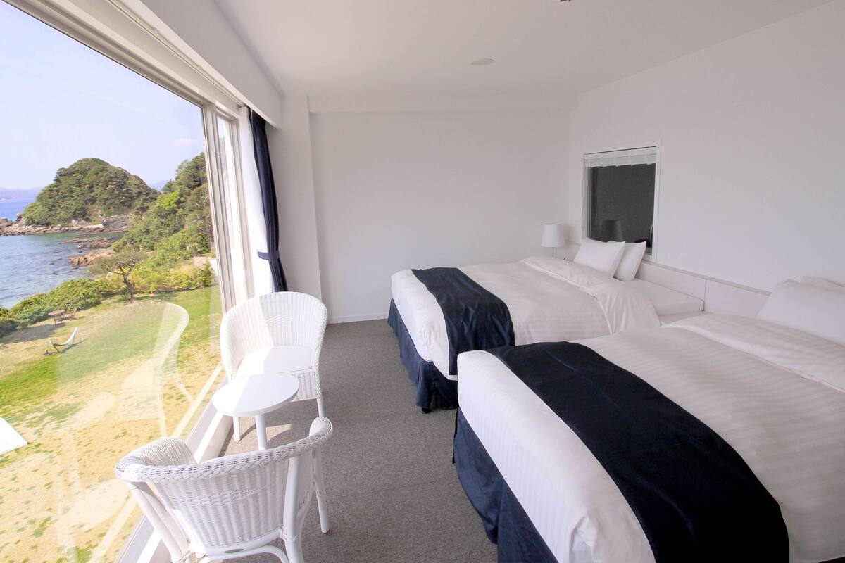 Ein Hotelzimmer mit zwei Betten, einem weißen Stuhl und einem großen Fenster mit Blick auf eine schöne Landschaft.