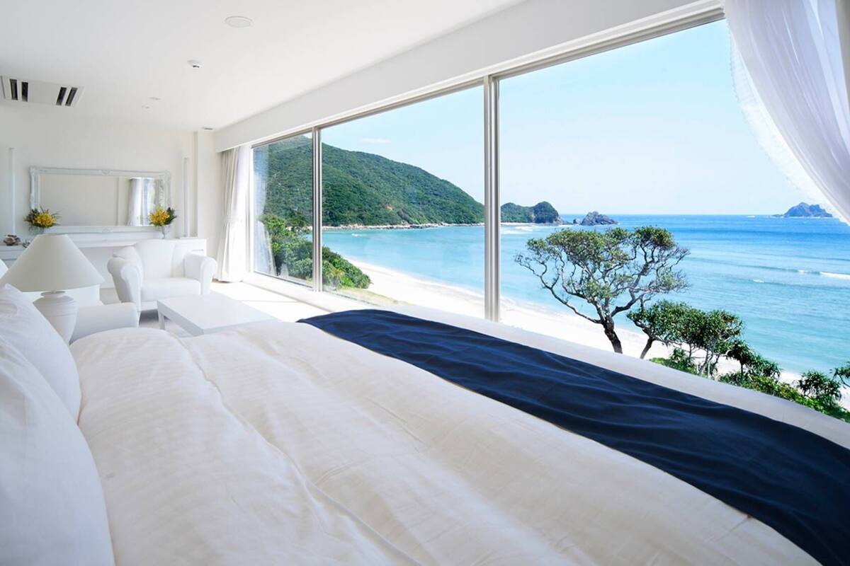 Ein Schlafzimmer mit einem großen Bett, einem Nachttisch, einer Lampe und Blick auf das Meer und einen Berg.