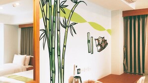 A hotel room with a wooden desk, a bed, and a wall with bamboo and tea set illustrations.