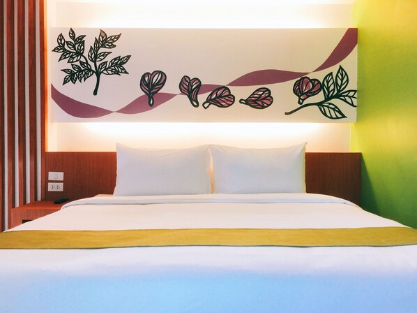 Habitación de hotel con cama, ropa de cama blanca, pared decorativa con motivos de hojas y cabecero de madera.