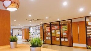 A modern hotel lobby with a wooden reception desk, potted plants, and a glass storefront displaying merchandise.