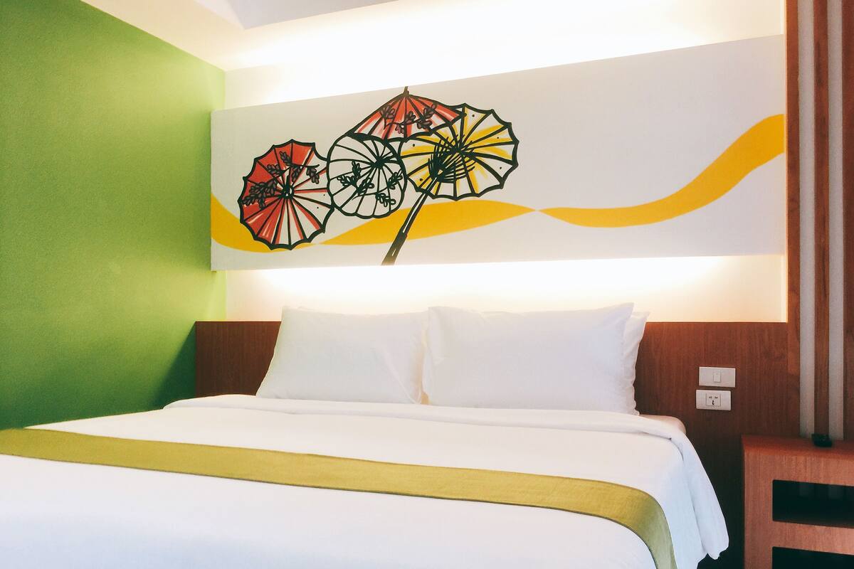 A hotel room with a bed, a nightstand, and a wall with a floral artwork.