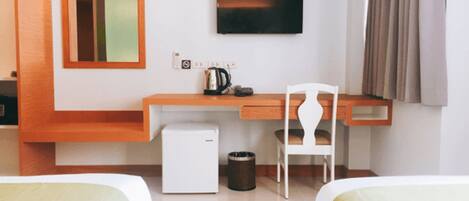 Habitación de hotel con un escritorio de madera, un refrigerador pequeño, una silla blanca, un televisor montado en la pared y dos camas con ropa blanca.
