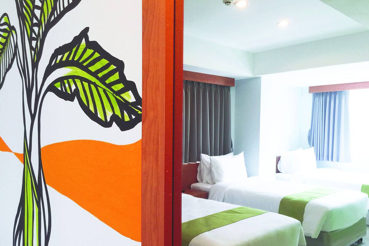 A hotel room with two beds, a large window with curtains, and a wall mural.