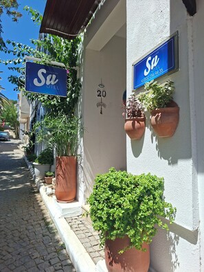 Ein Gebäude mit einem Schild, auf dem 'Su HOTEL' und die Zahl '20' stehen. Vor dem Eingang befinden sich Blumentöpfe.
