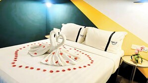 A hotel room with a bed, pillows, a bedside table with a vase, and a wall with a light fixture. - Smile Hotel Cheras Sri Permaisuri (Kuala Lumpur)