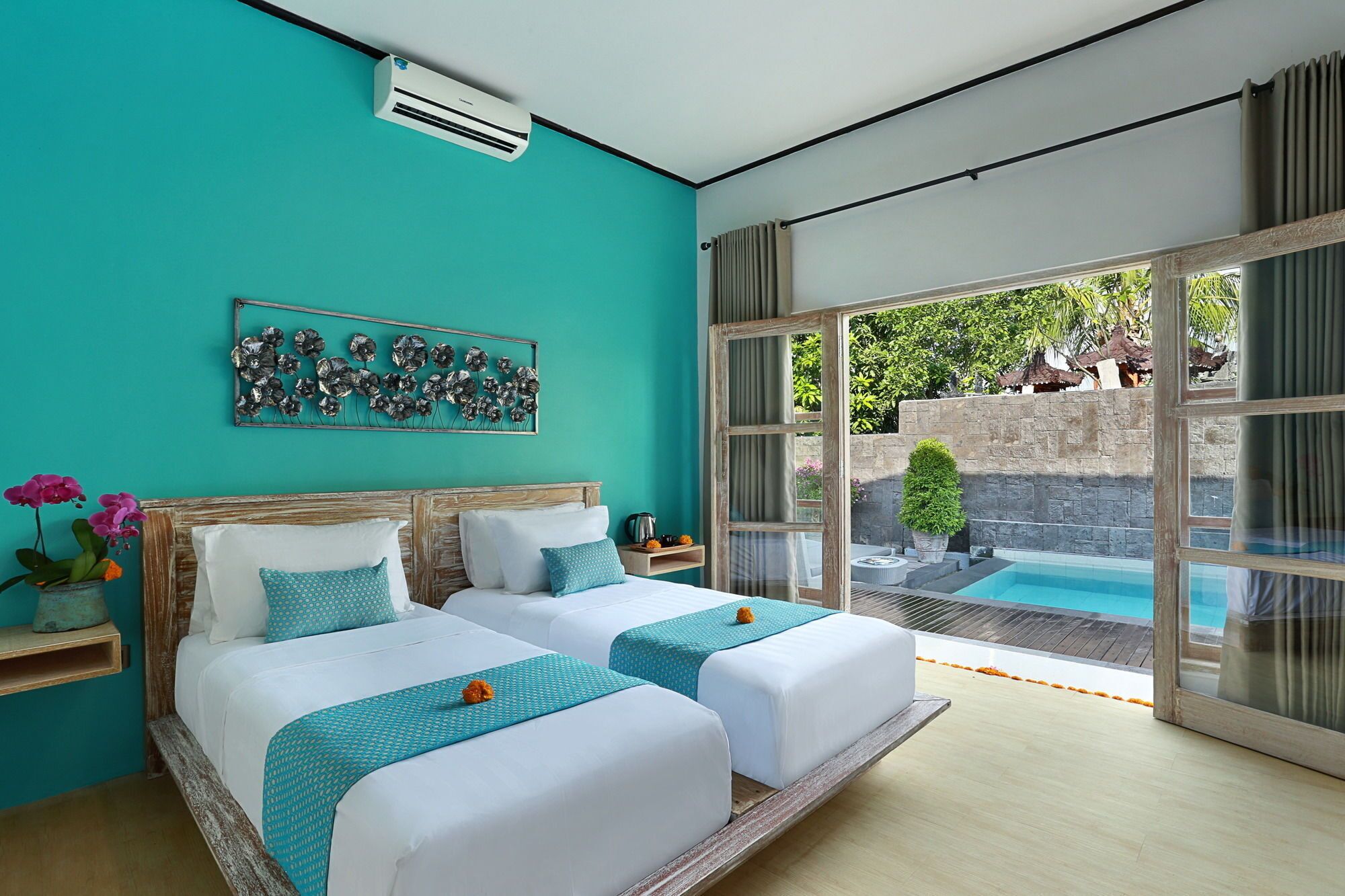 Habitación de hotel con dos camas, un ventanal con vistas a una piscina y zona exterior, y una pieza decorativa de metal en la pared.