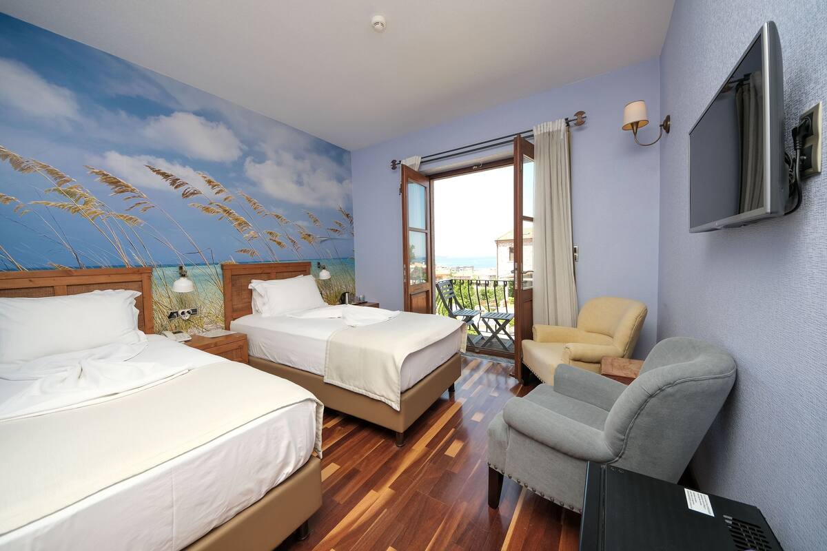 A hotel room with two beds, a TV, a chair, and a balcony with a view.
