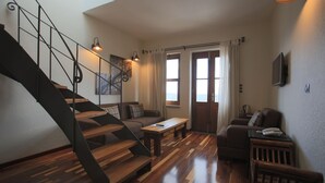 A modern living room with a wooden staircase, a sofa, a coffee table, and a television mounted on the wall. - Cunda Labris Hotel (Ayvalik)