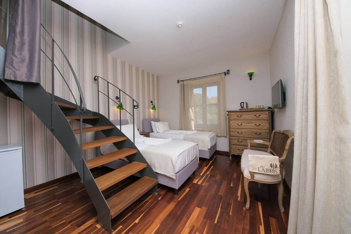 A bedroom with a wooden staircase, two beds, a dresser, a chair, and a television.