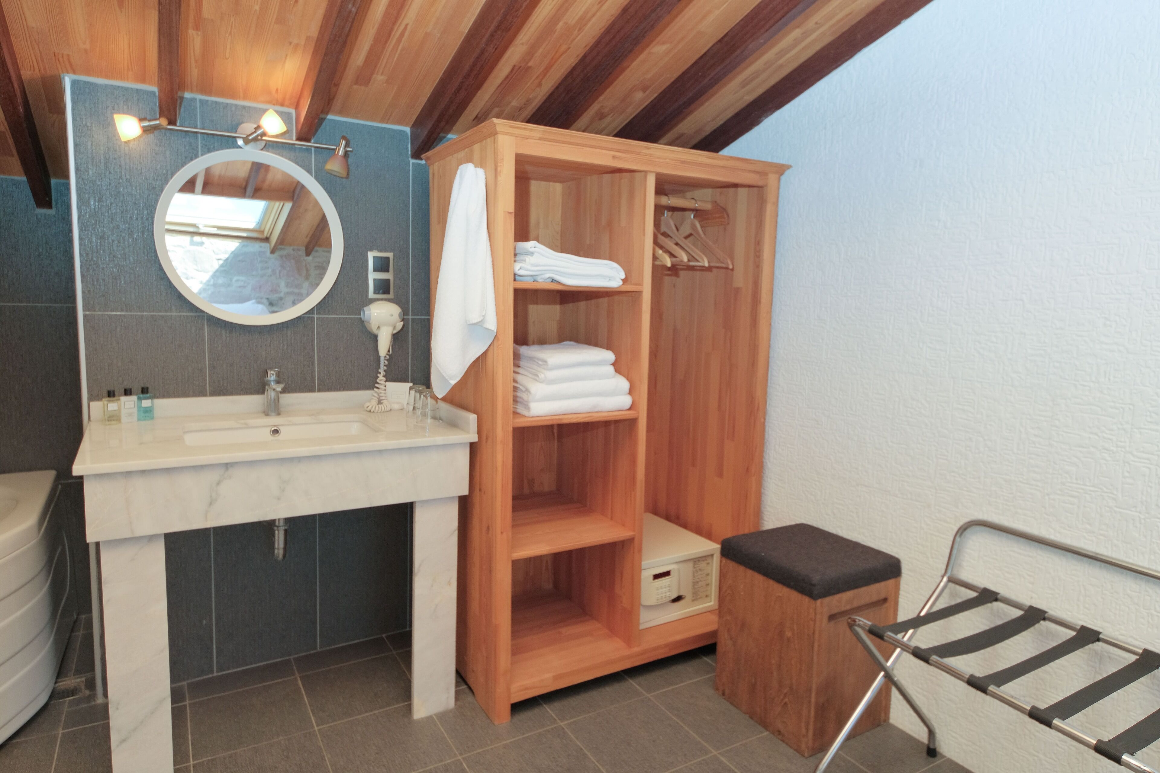 A modern bathroom with a wooden vanity, a round mirror, and a built-in shelf for towels.
