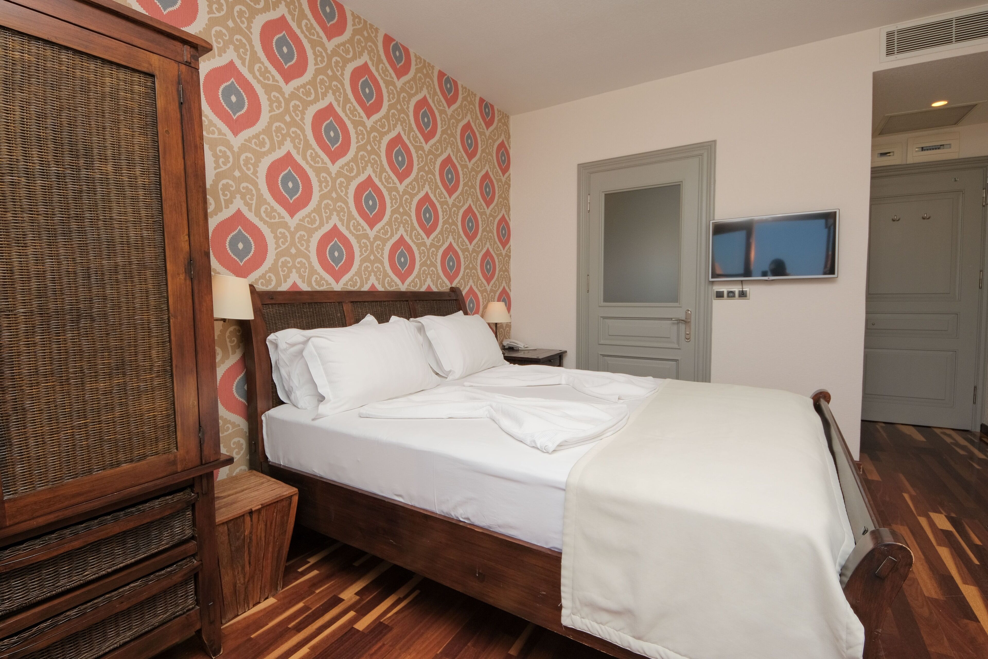 Un letto rifatto con lenzuola bianche, una testiera in legno e una carta da parati decorata.