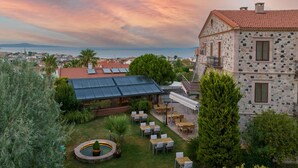 A courtyard with outdoor seating, a stone building, and a view of the sea. - Cunda Labris Hotel (Ayvalik)