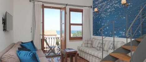 A living room with a sofa, a small table, a staircase, and a view of the sea.