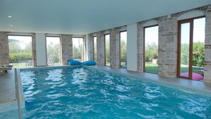 An indoor swimming pool with clear glass walls, blue bean bags, and a view of greenery outside. - Cunda Labris Hotel (Ayvalik)