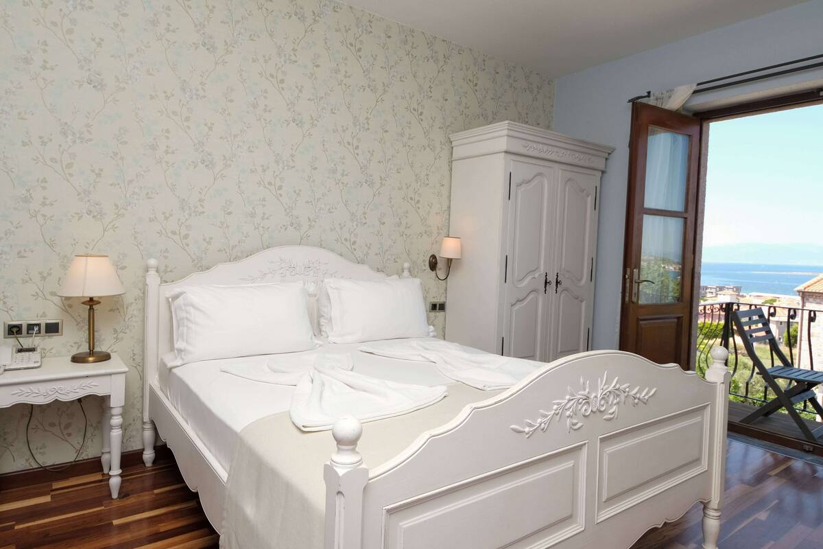 A bedroom with a bed, bedside table, lamp, wardrobe, and a balcony with a view.