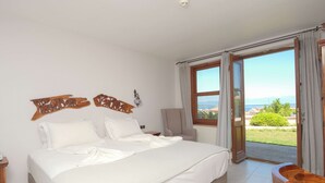 A bedroom with a large bed, a wooden headboard, a chair, and a view of the outdoors through a glass door. - Cunda Labris Hotel (Ayvalik)