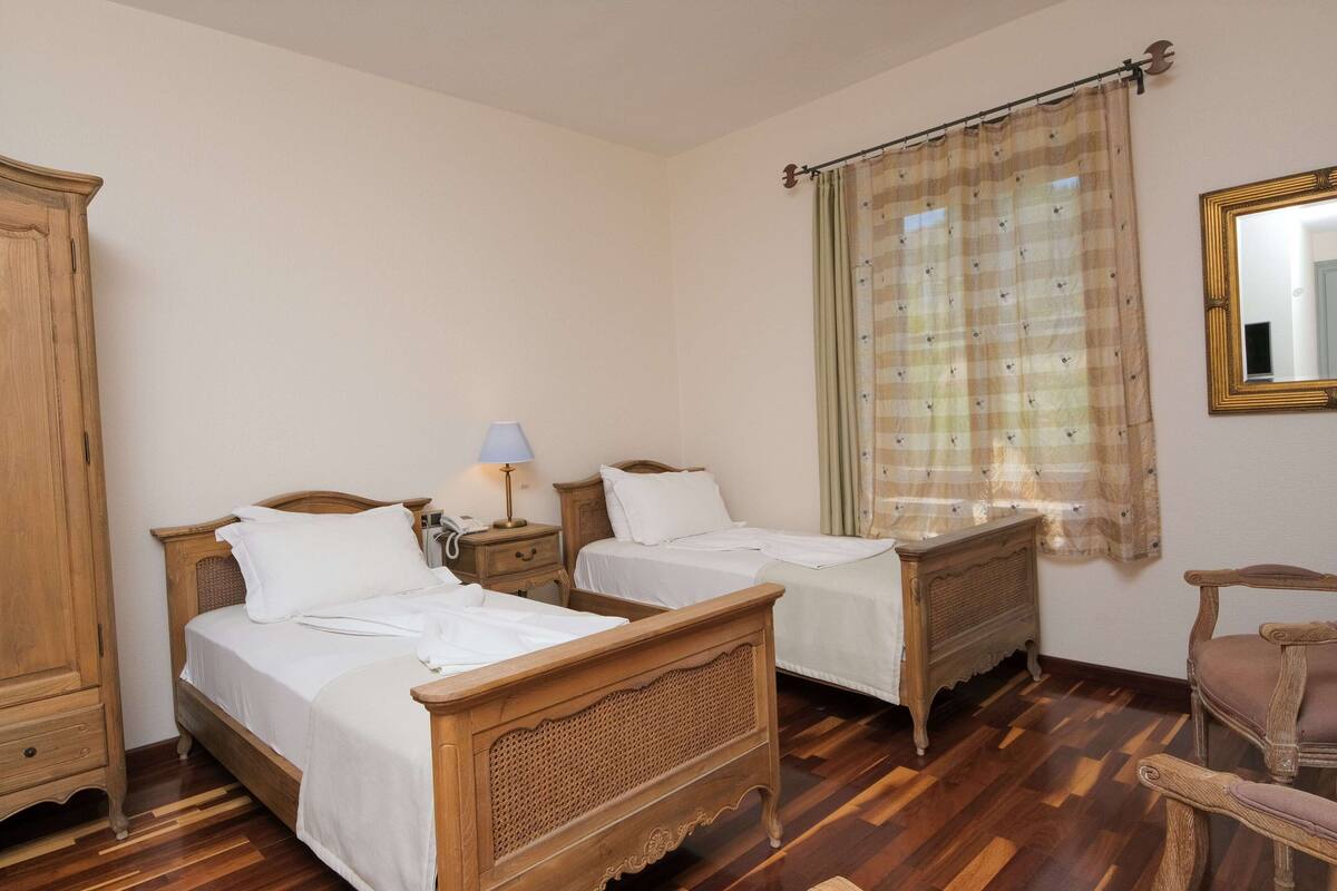 A bedroom with two wooden beds, a nightstand with a lamp, a wardrobe, and a chair.