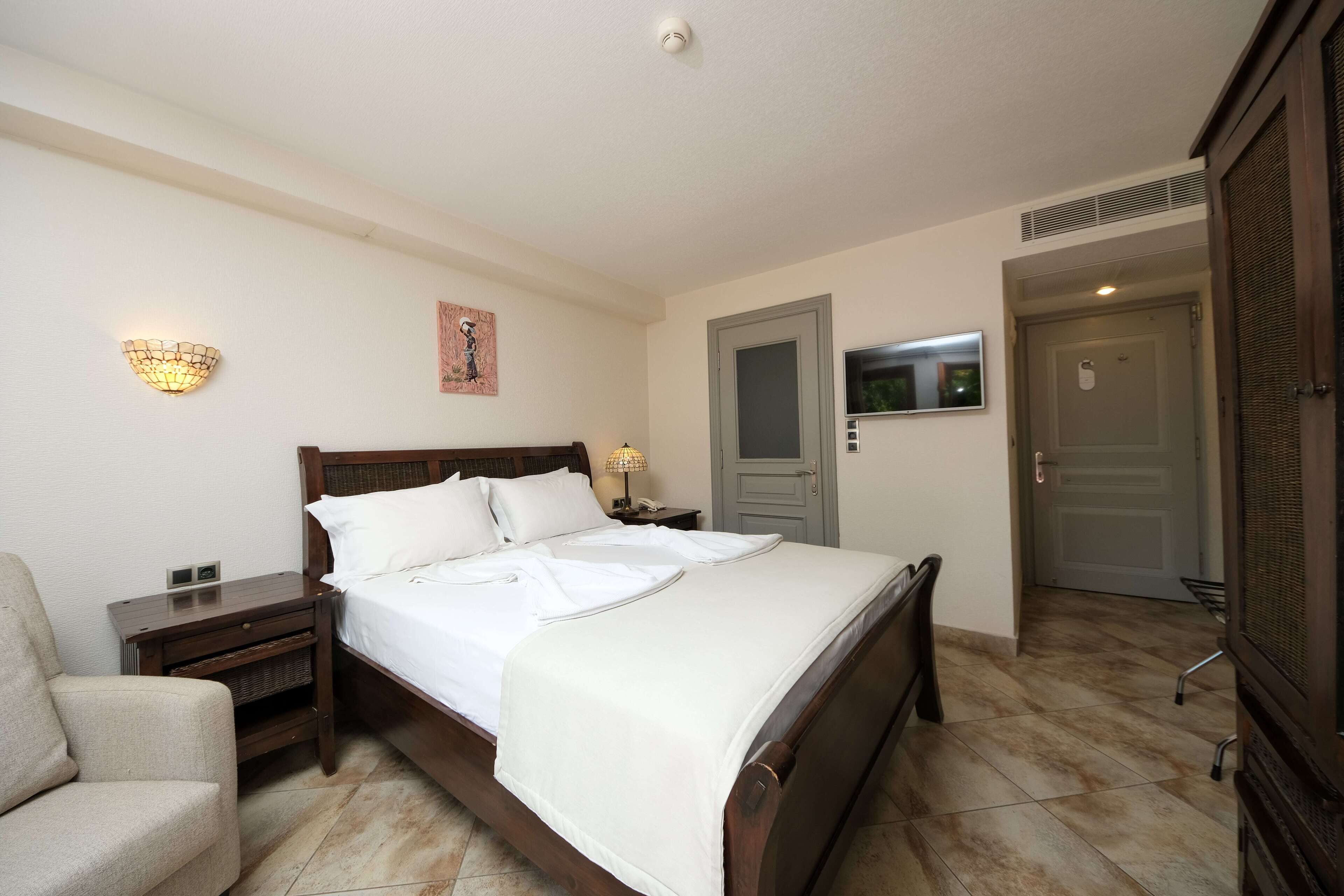 A neatly arranged bedroom with a bed, bedside tables, a chair, a TV, and a door.