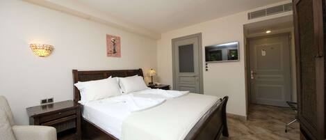 A neatly arranged bedroom with a bed, bedside tables, a chair, a TV, and a door.