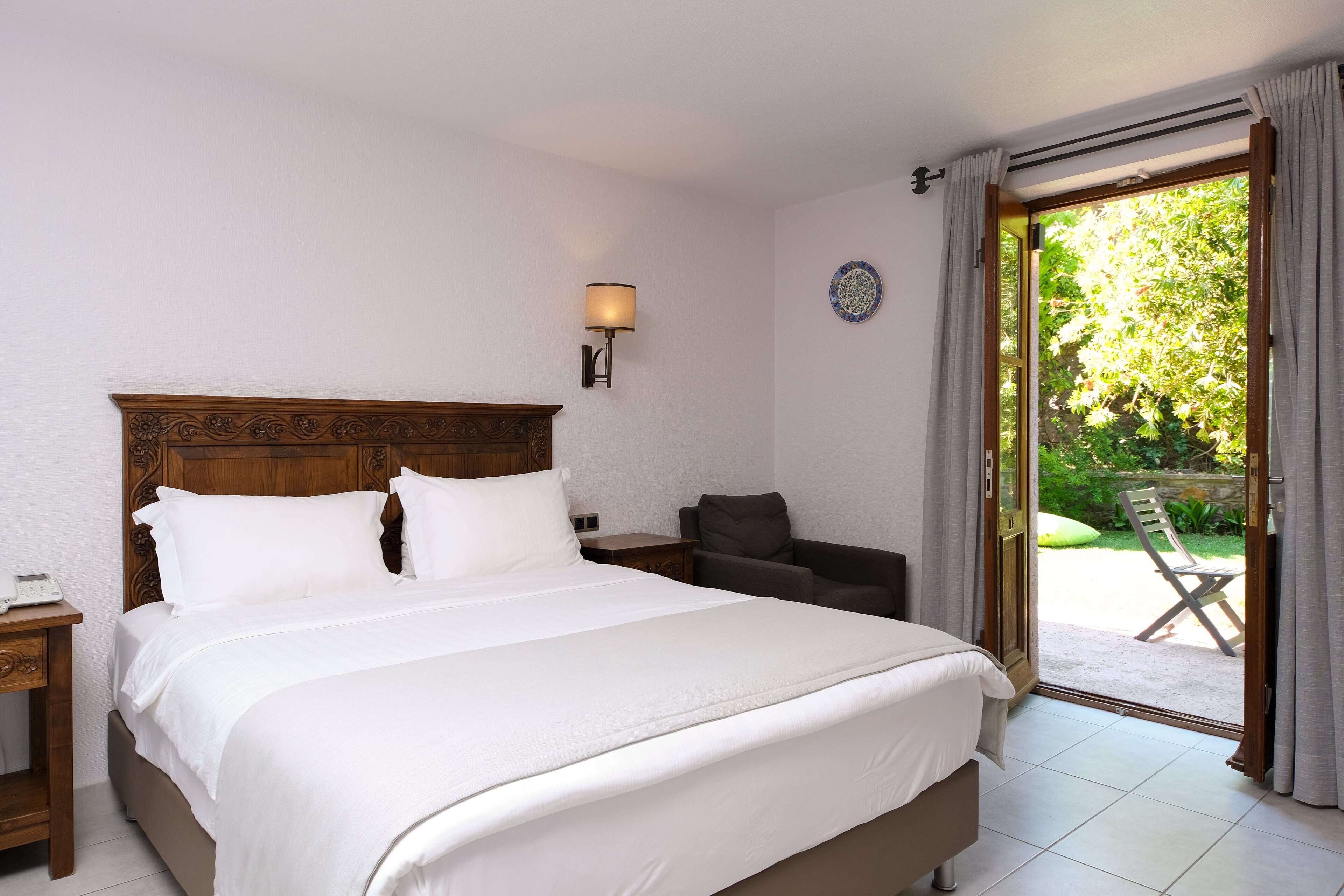 Une chambre d’hôtel avec un grand lit, une table de chevet avec une lampe, une chaise et une vue sur l’extérieur grâce à une porte coulissante.