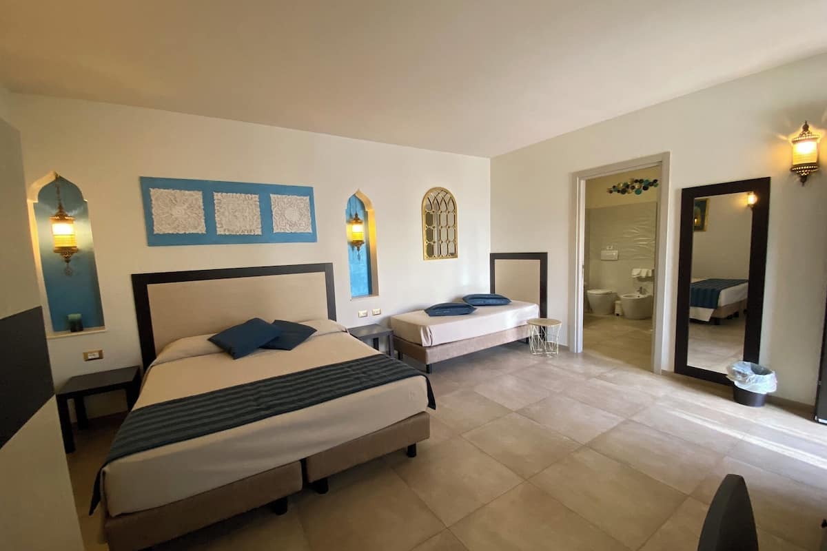 A hotel room with a large bed, a smaller bed, a bedside table, a mirror, and a bathroom visible through an open door.