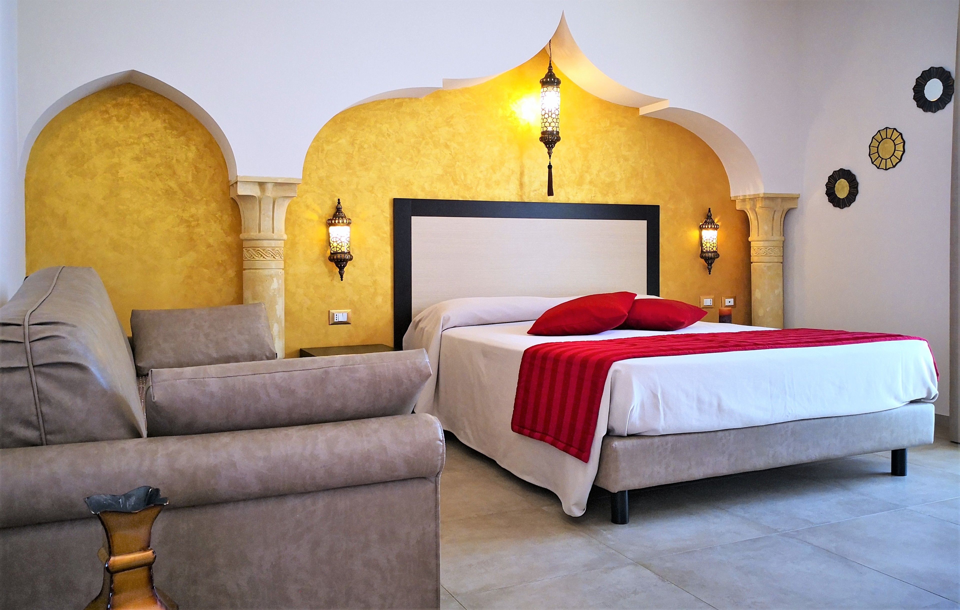 A bedroom with a bed, two wall-mounted lamps, a sofa, and a decorative wall arch.