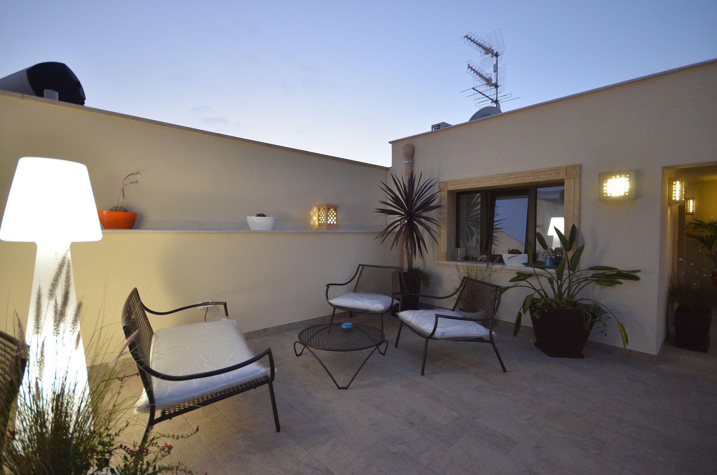An outdoor patio area with a seating arrangement, potted plants, and a window with a view.