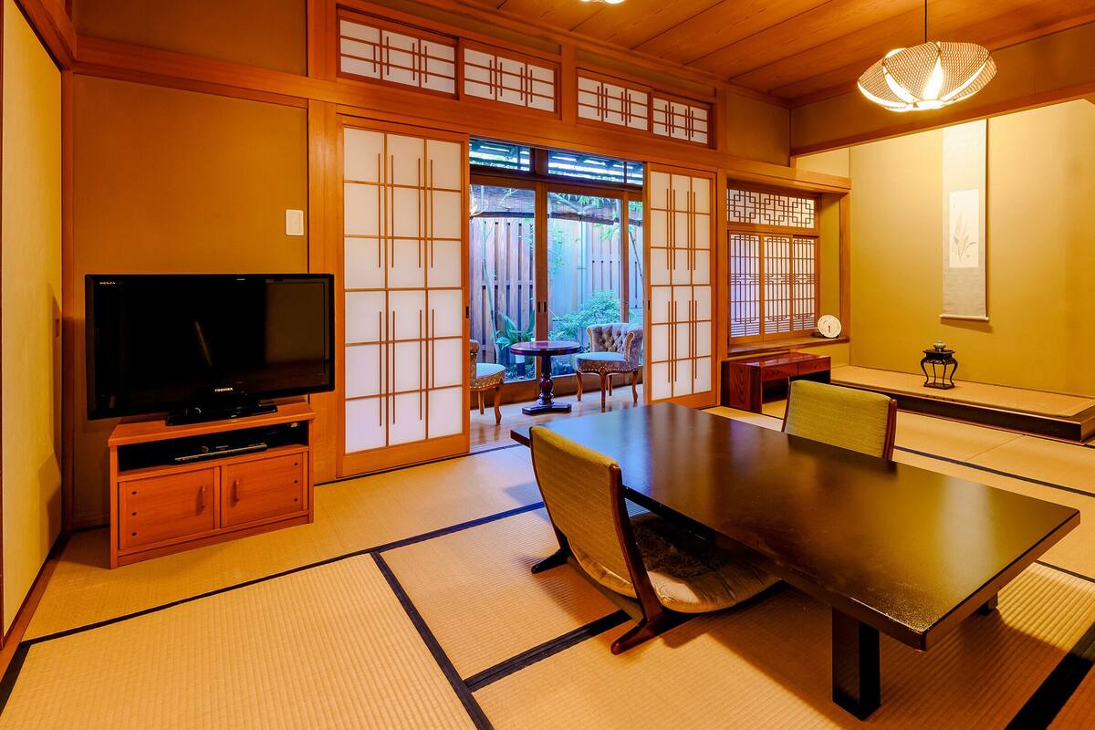 A traditional Japanese room with tatami flooring, a low table, and a television on a wooden stand.
