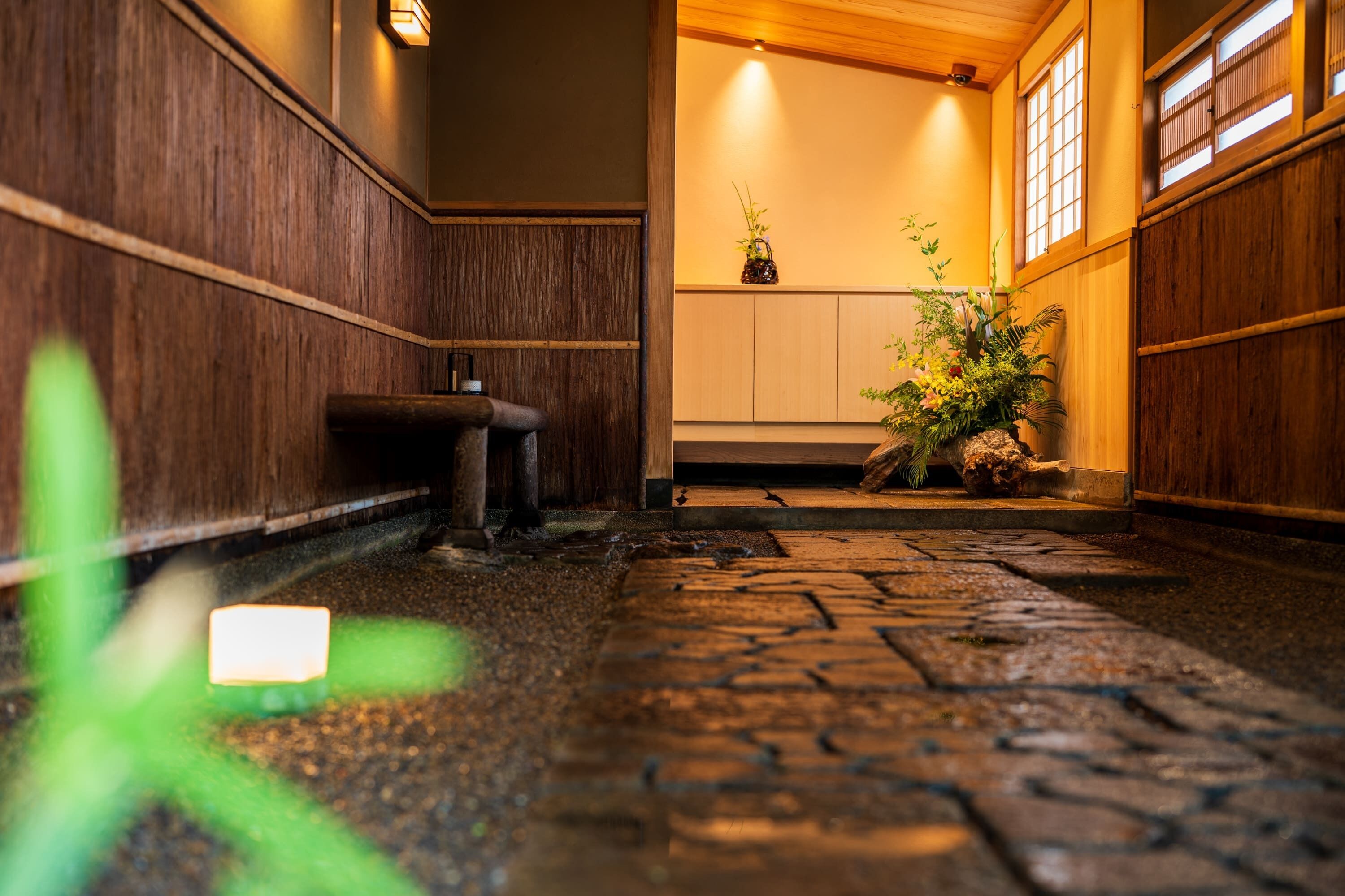 A traditional Japanese interior with wooden paneling, a stone floor, and a small plant arrangement.