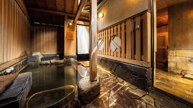 Un onsen japonais traditionnel, avec un sol en pierre, des murs en bois et un espace de baignade en pierre.