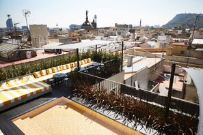 Eine Dachterrasse mit Sitzgelegenheit, einem kleinen Tisch und Blick auf die Stadt.