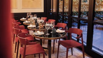 Comedor con mesas redondas, sillas rojas y vistas al exterior a través de amplios ventanales.