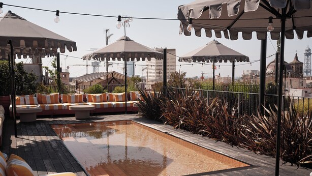 Un espacio al aire libre con cojines a rayas, una pequeña piscina y sombrillas que dan sombra.