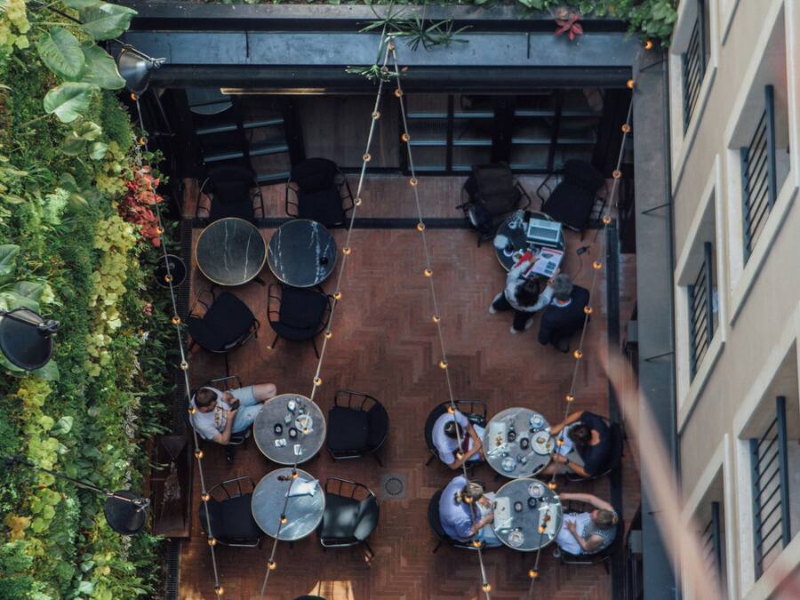 An outdoor patio with tables and chairs, surrounded by lush greenery and plants.