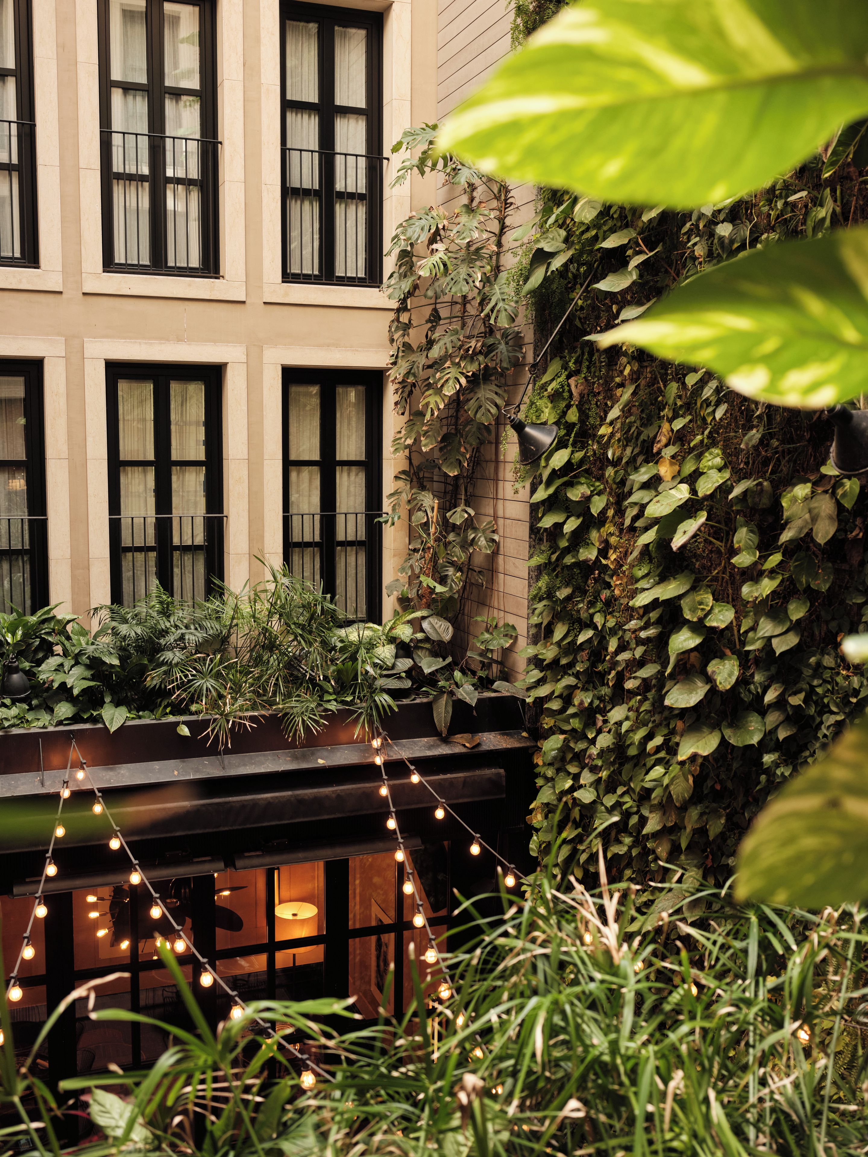 Un immeuble doté de nombreuses fenêtres, d’un balcon orné de plantes et de guirlandes lumineuses.