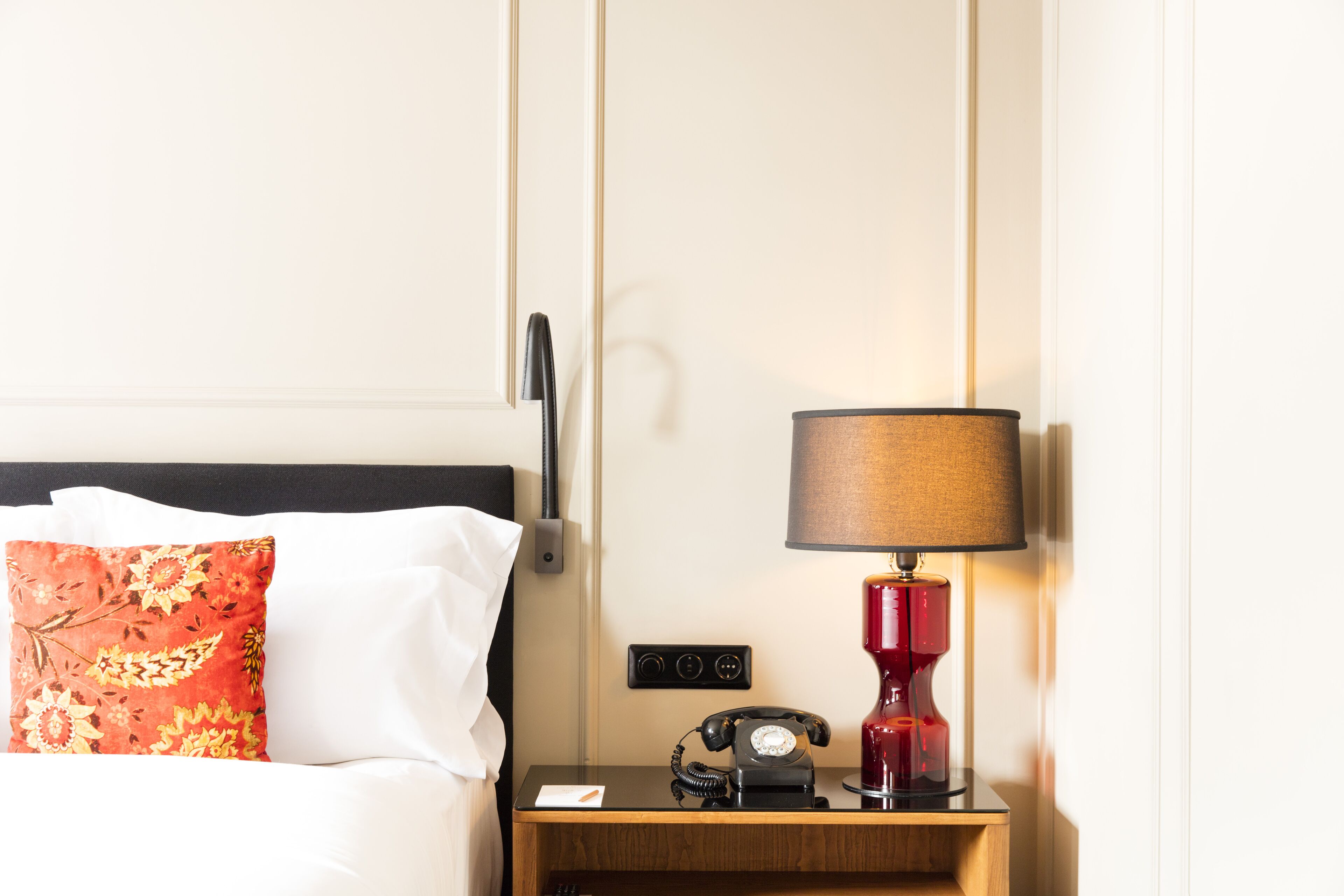 A hotel room with a bed, a nightstand, a telephone, and a lamp.