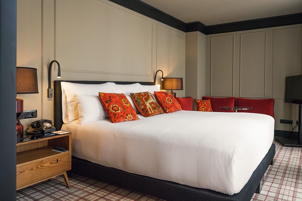A hotel room with a large bed, a wooden nightstand with a telephone, and a TV on a stand.