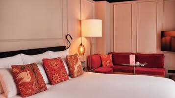 A hotel room with a large bed, a red sofa, a small table, and a wall-mounted TV.